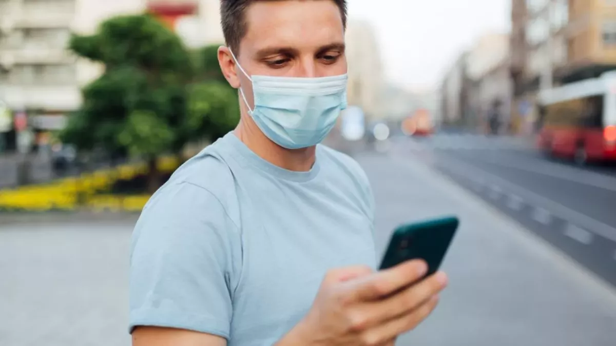 Un homme masqué consulte son smartphone dans la rue 