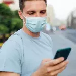 Un homme masqué consulte son smartphone dans la rue 